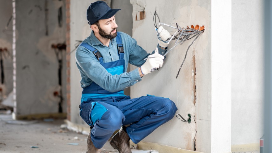 Instalator elektryk wyprowadza kable elektryczne ze ściany pod gniazdka natynkowe